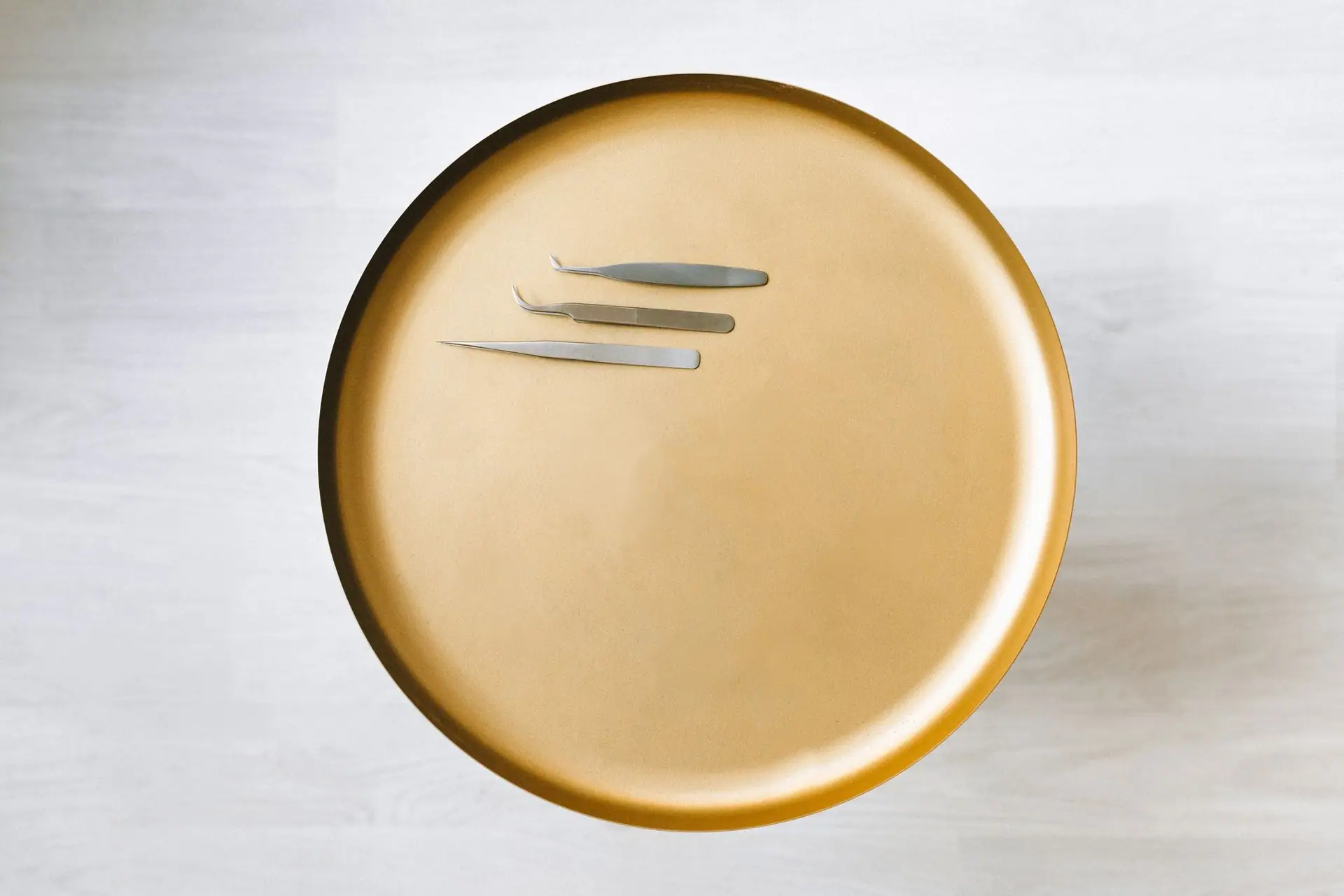Stainless steel tweezers on a brushed gold tray