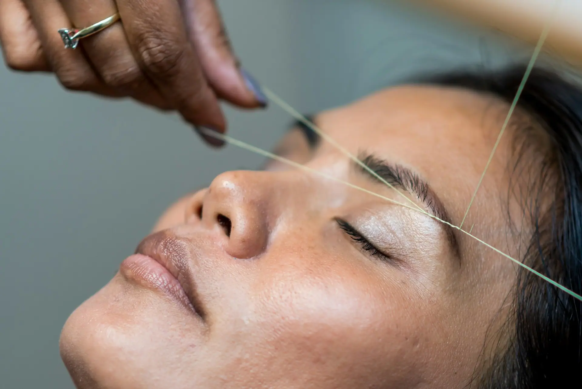 Close-up of eyebrow threading with the thread pulled across the brow