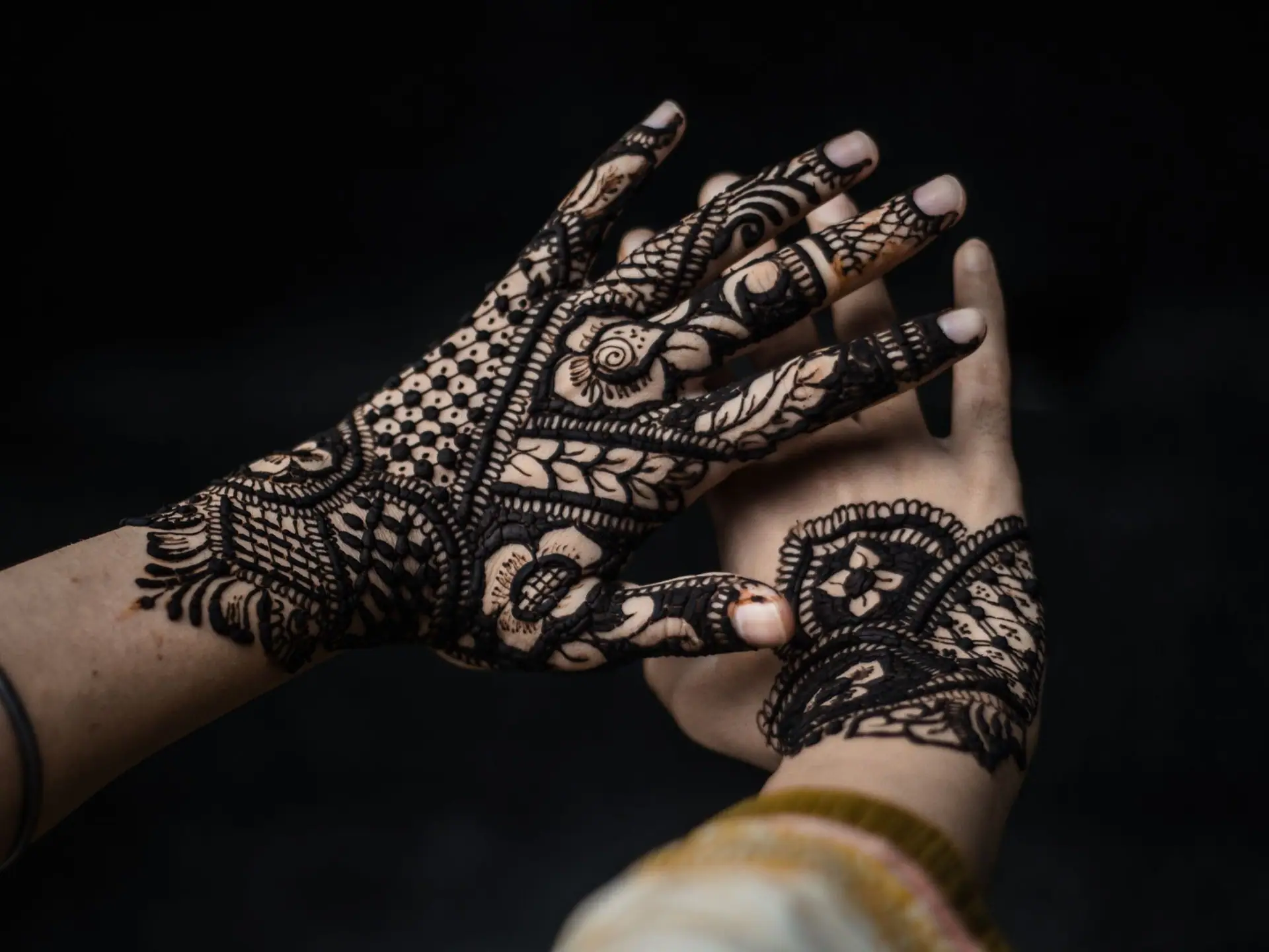 Hands with detailed henna designs on a black background