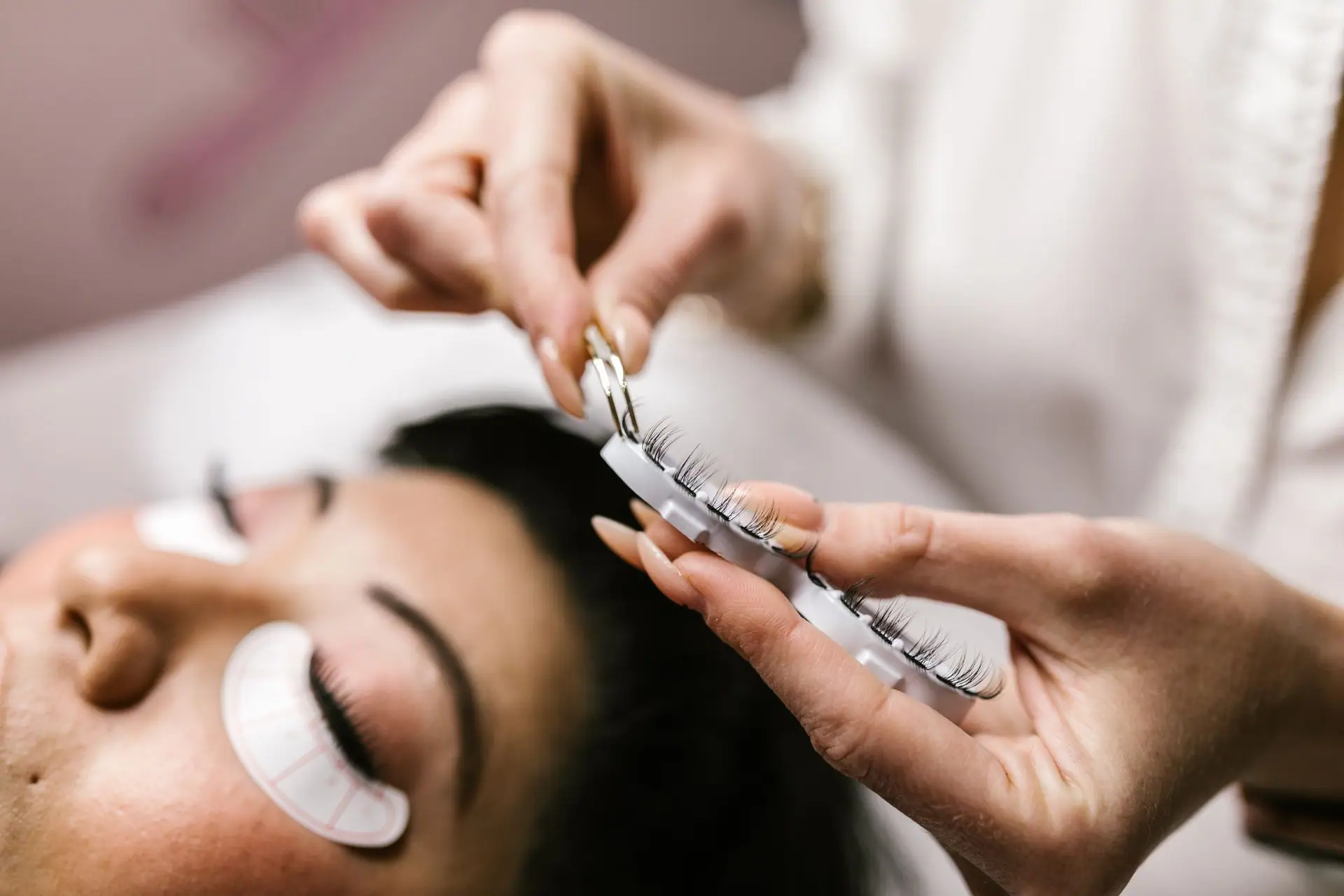 Lash extensions being picked from a tray above a client with under-eye pads